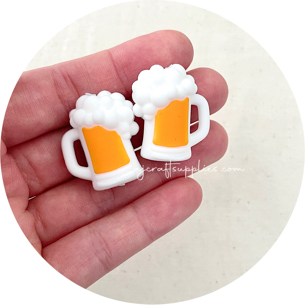 Two beer mug-shaped charms held in a hand with a white background.